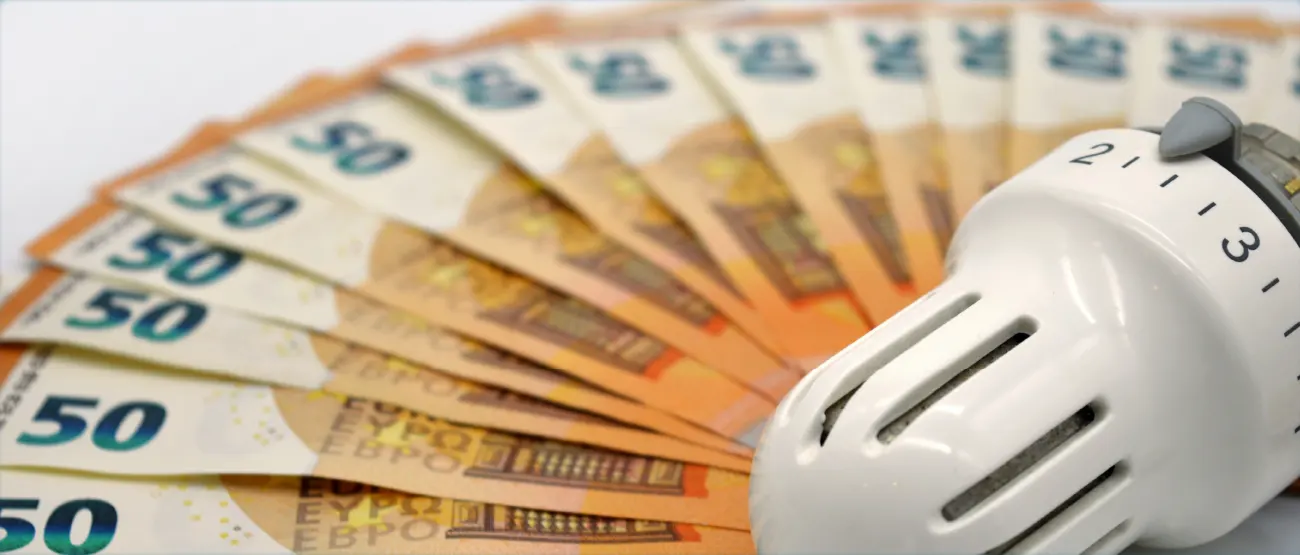 Ein Heizungsthermostat liegt auf mehreren aufgefächerten 50 Euro-Gedscheinen