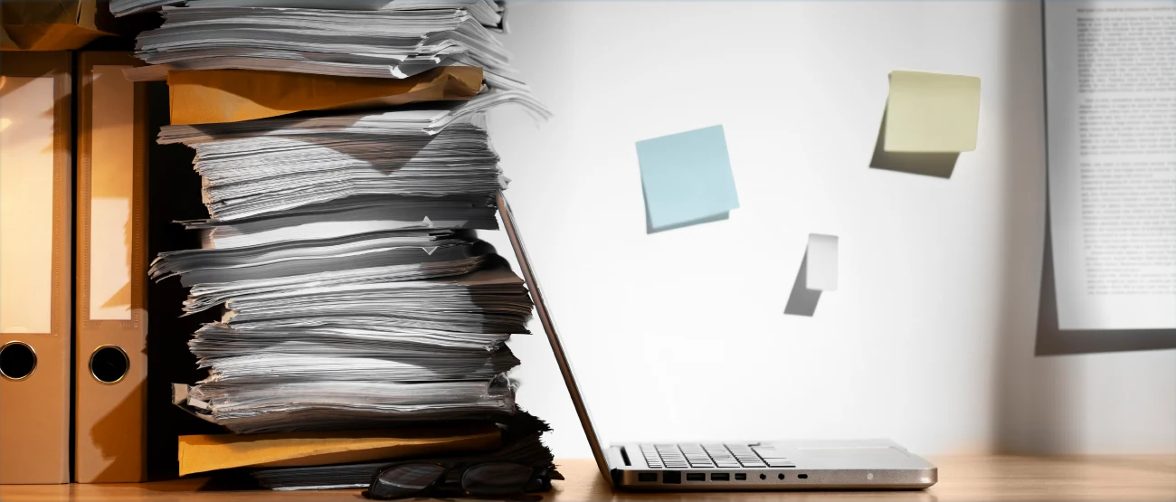 Ein aufgeklapptes Notebook steht neben einem Stapel Akten die um Ordner angeordnet sind